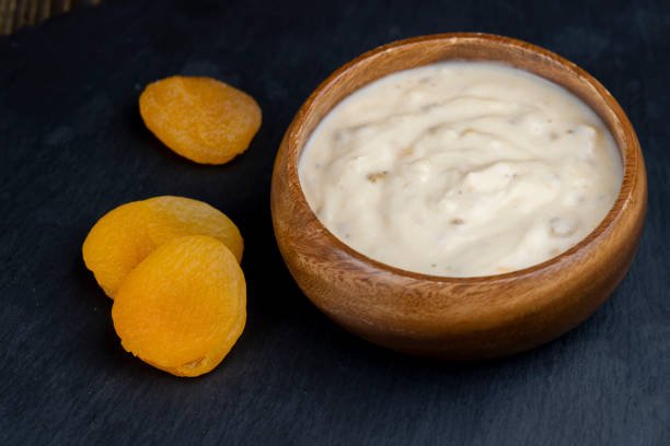 A bowl of creamy yogurt topped with dried apricots, set against a sleek black background.