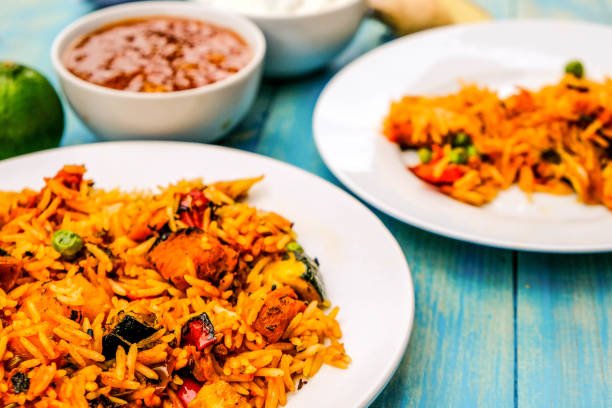 A plate of vibrant Mexican rice with assorted vegetables include apricot dry fruit, accompanied by a bowl of fresh salsa.