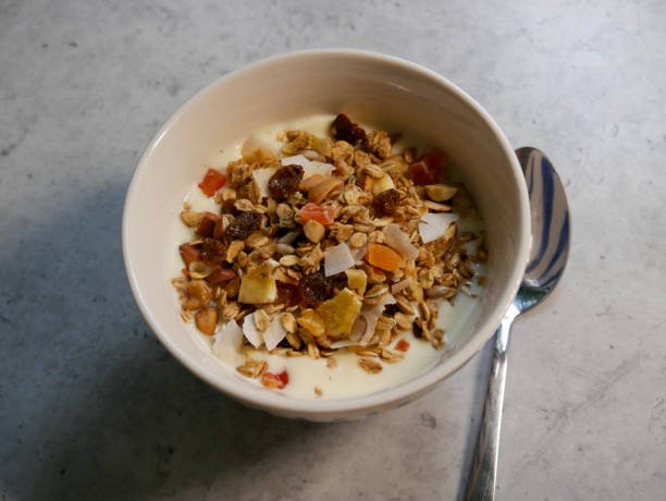 A bowl of apricot dry fruit granola topped with yogurt and fresh fruit, showcasing a healthy breakfast option.
