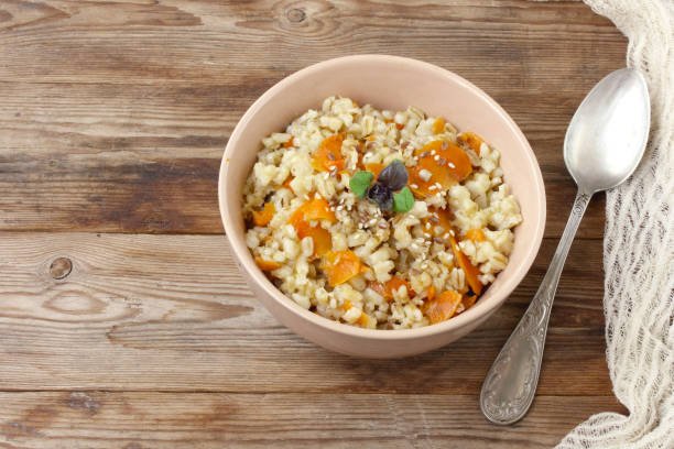 Barley porridge topped with pumpkin and sesame seeds, accompanied by a vibrant apricot dry fruit and quinoa salad.