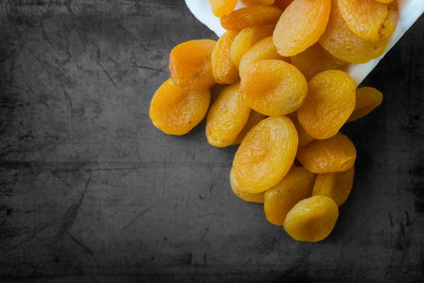 Dried apricots arranged on a black background, showcasing their vibrant orange color and unique texture.