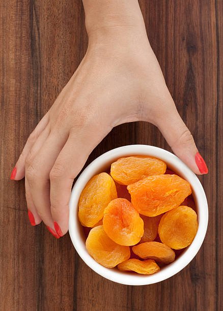 A person gently holds a bowl filled with ripe, orange apricots, showcasing their vibrant color and fresh appearance.