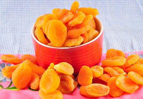 A bowl filled with dried apricots placed on a wooden table, showcasing their rich orange color and natural texture.