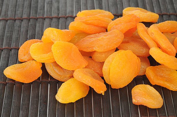 A close-up of dried apricots arranged neatly on a bamboo mat, showcasing their rich color and texture.
