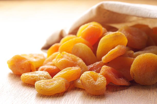 A bag of dried apricots placed on a wooden table, showcasing its vibrant orange color and natural texture.