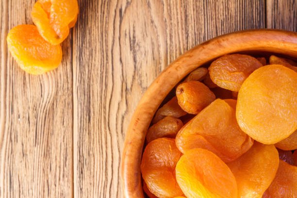 A bowl of apricot dry fruit placed on a rustic wooden table, showcasing their vibrant orange color and natural texture.