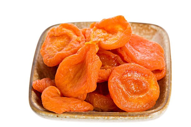 A bowl filled with dried apricots placed on a clean white background, showcasing their rich color and texture.