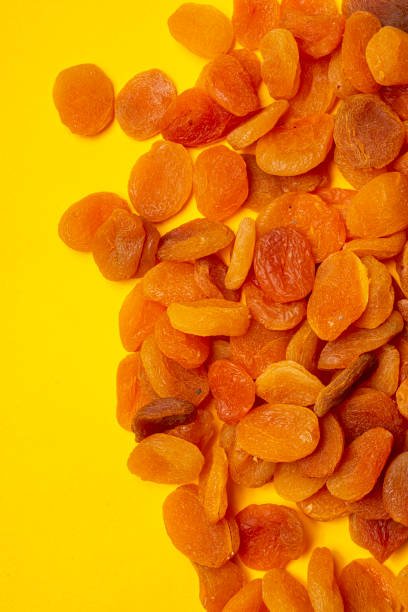 Dried apricots arranged on a vibrant yellow background, showcasing their rich color and texture.