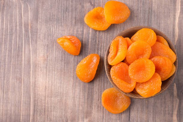 A rustic wooden bowl containing dried apricots, displayed on a weathered wooden background, emphasizing a natural aesthetic.