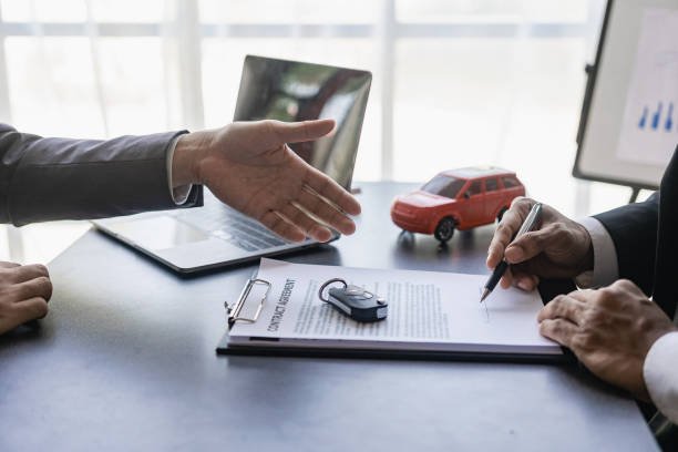 Two business professionals shaking hands over a car, symbolizing a successful agreement related to car insurance.