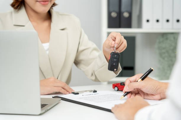 A woman holds a car key in front of a laptop, symbolizing the connection between car ownership and insurance management.