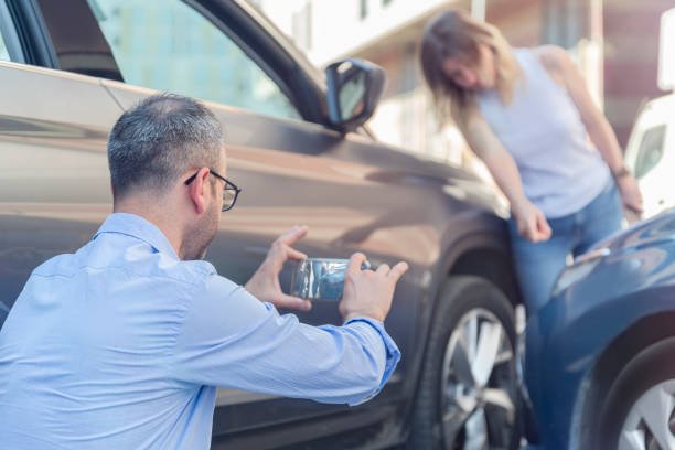 A man photographing a car accident scene, highlighting the importance of auto insurance in such situations.